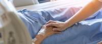 Caregiver holding elderly senior patient hand in hospital bed or nursing hospice, geriatrician palliative home,